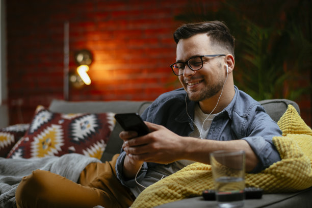 英俊的年轻人在沙发上休息，看他的智能手机。图片下载