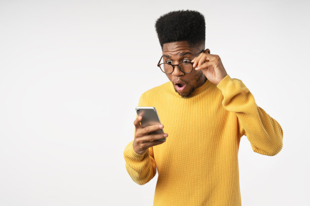 一名非洲男子在用智能手机看孤立的白色背景时震惊的脸图片下载