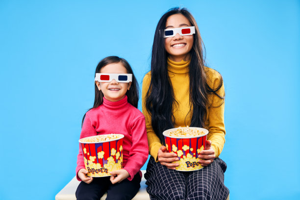 快乐微笑的妈妈和她的小女儿在3D眼镜与爆米花看电影图片下载
