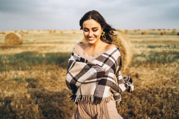 一个漂亮的黑发女人的肖像穿着裙子和一个温暖的格子。一个女人正带着干草在麦田里散步图片下载