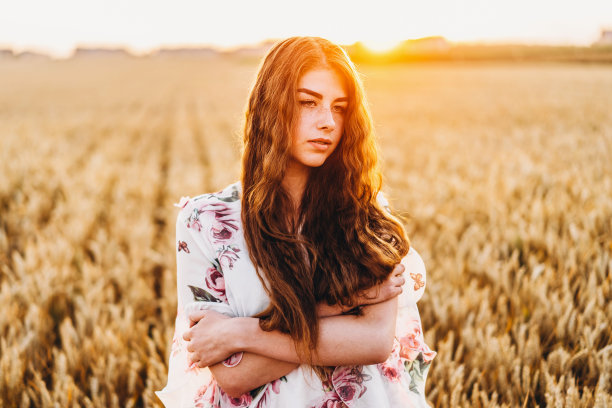 令人难以置信的年轻女子，长着长长的卷发，脸上有雀斑。日落时分，在麦田里摆姿势的女人。特写肖像图片下载