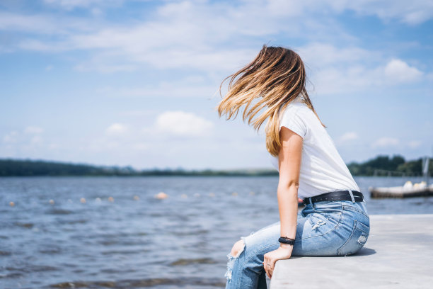 戴着时尚眼镜的长发年轻女子在湖边摆造型。穿着牛仔裤和t恤的女孩微笑着看向别处图片下载