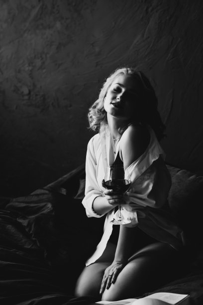 孤独美丽的女人在卧室的床上用一杯红酒放松。低调的黑白艺术照片。软选择聚焦。图片下载