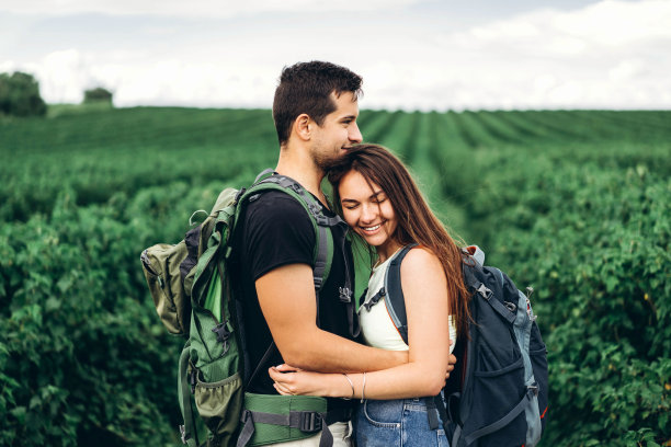 这是一对快乐的年轻夫妇在春天的球场上背着背包的照片。男人和女人在醋栗种植园里散步图片下载