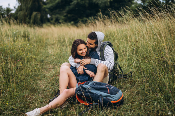 长发女子和背着背包坐在森林草地上的男子。享受大自然的乐趣，拥抱和亲吻图片下载