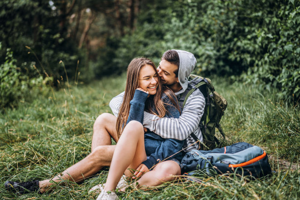 长发女子和背着背包坐在森林草地上的男子。享受大自然的乐趣，拥抱和亲吻图片下载