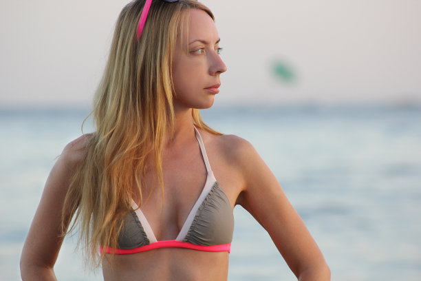 美丽的女孩穿着两件套泳衣正侧身站在海边，模糊了灯光的背景图片下载