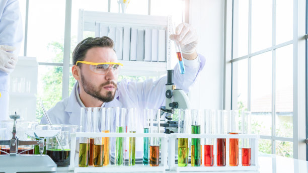 男性科学家拿着一根装有液体物质的管子。液体物质的试管和烧杯的研究正在实验室中进行。图片下载