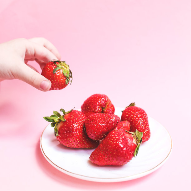 俯视图Childs手持一个草莓在粉红色的背景，盘子草莓。夏季健康饮食理念。图片下载