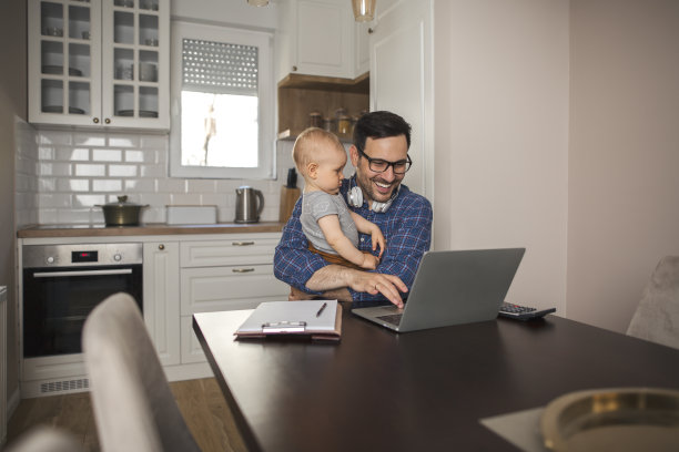 一位父亲抱着他的宝贝儿子在电脑上远程工作。图片下载