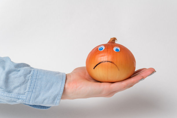 手持白色背景上的大洋葱。带着悲伤的微笑和大眼睛鞠躬图片下载