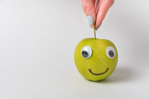 手指拿着苹果的茎。白色背景上的苹果笑脸。图片下载