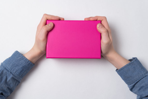 孩子们的手拿着一个白色背景上的粉色硬纸盒。前视图。礼物送给女孩。图片下载