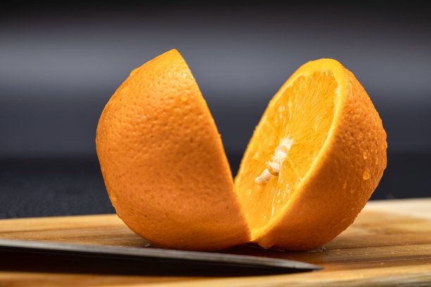 在木板上切橘子。鲜橙水果放在切菜板上做沙拉或榨汁。健康饮食、烹饪、节食的概念。靠近切片的橙子。图片下载
