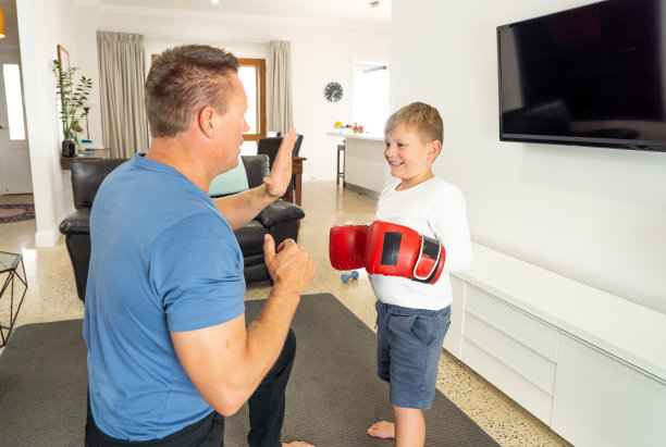 COVID-19 lockdon。在冠状病毒隔离期间，父亲和儿子一起玩拳击，在家锻炼身体。呆在家里，锻炼，健康在保持社交距离期间自我照顾。图片下载