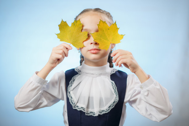 小学生把脸藏在秋叶后面图片下载