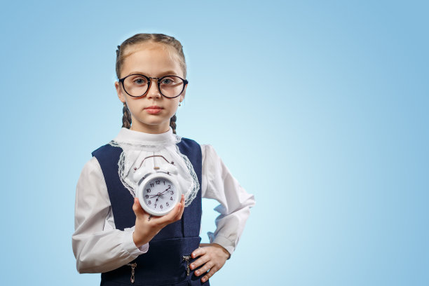 空闲时间的概念。准备上第一课。可爱的，甜美的，可爱的，美丽的，漂亮的小女孩孤立在生动的黄色背景与大闹钟在她的手图片下载