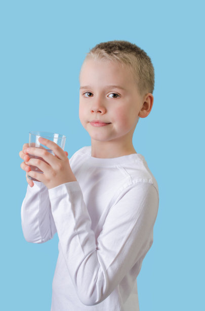 孩子手里拿着一杯水。金发小男孩拿着水杯，看着镜头。图片下载