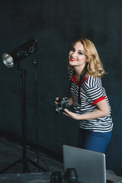 年轻美丽的女孩摄影师手拿照相机在摄影工作室使用人工照明工作。妇女的工作是一种爱好。软选择聚焦。图片下载