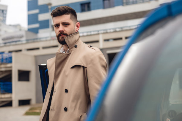 在户外穿着米色夹克的胡子英俊男子的肖像。在城市街道上复制空间的经营理念。蓝色车旁边的人图片下载