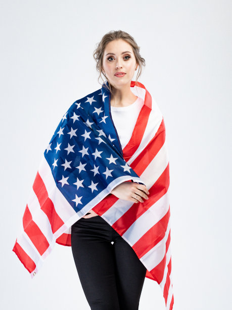 时尚年轻女子的肖像在工作室白色衬衫与灰色孤立的背景。概念与复制空间。她手里拿着一面美国国旗图片下载