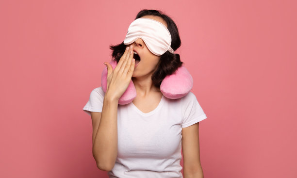 低能量。一个穿着睡衣的年轻女人的特写照片，她有一个脖子上的枕头在她的肩膀上，打哈欠无休止。图片下载