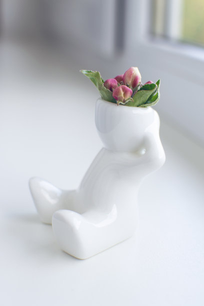 白色的头上戴着苹果花蕾的陶制人像正坐在窗台上图片下载