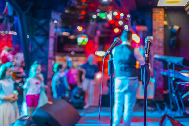 舞台上有两只麦克风，男主持人在后台，一群孩子在一起玩耍。水平图像组成。水平的形象定位图片下载