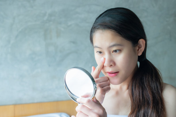 漂亮的亚洲女人的肖像看和检查她的脸后化妆的迷你镜。图片下载