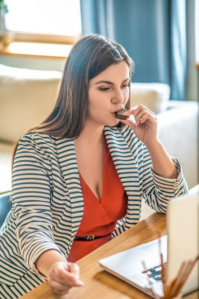 穿着条纹夹克的年轻女子一边吃一边看图片下载