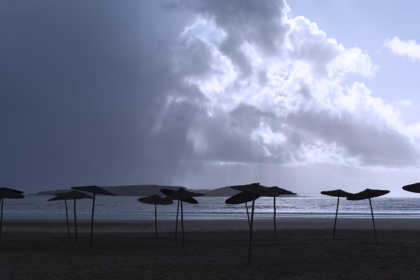 空旷的海滩和遮阳伞对抗黑暗多云的天空。图片下载