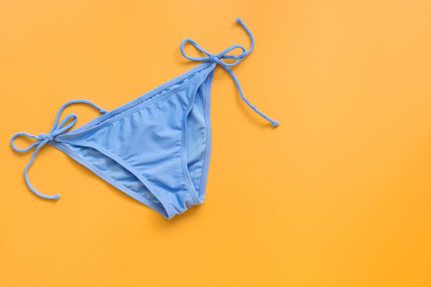 淡黄色背景上的海滩蓝色比基尼。女性性感的多色比基尼短裤或内裤。暑假的概念。俯视图，平放，复制空间。图片下载