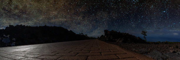 星空下的一条山路，在银光下闪烁着一轮巨大的明月。在散落的星团和星云的背景下，一棵孤独的松树在一条冰冻的熔岩流上图片下载