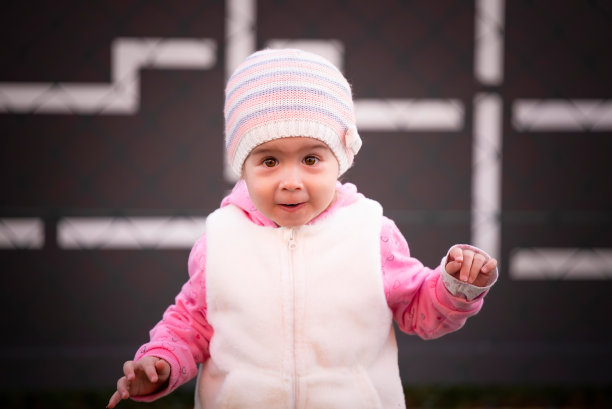 可爱的2岁白人小女孩跑向后院的摄像机，戴着帽子。图片下载