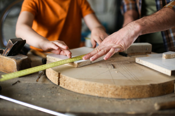 快乐的年轻男木匠教他的儿子在他的车间与木材工作图片下载