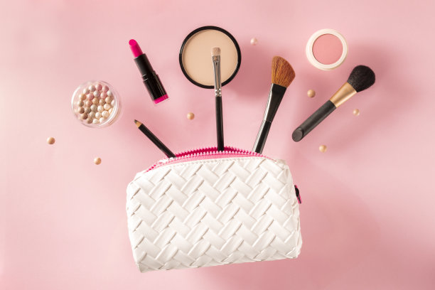 专业的化妆品，从包里飞出来，粉红色的背景。口红，刷子，粉盒，创意的美丽设计图片下载