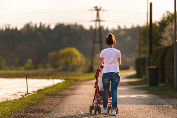 日落前在乡村地区户外推着红色婴儿车的年轻母亲和孩子图片下载