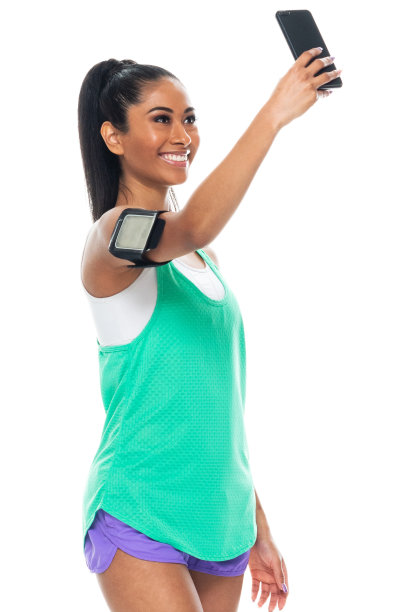 z一代年轻女性穿着运动鞋，用智能手机站在黑色背景前拍照图片下载