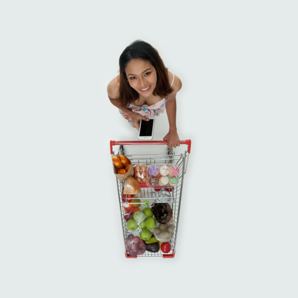 年轻女性站在白色背景前，拿着杂货，用着智能手机图片下载