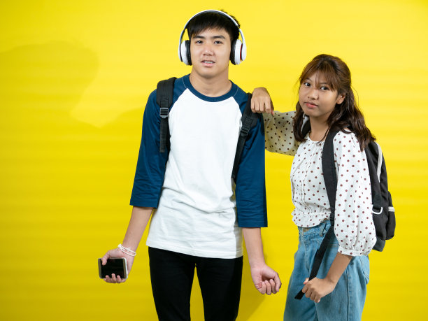 亚洲少年男孩和女孩与背包在黄色的背景。图片下载
