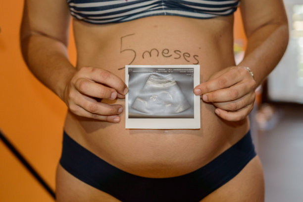 美丽的怀孕5个月的妇女显示她的超声波在她的手旁边的腹部。图片下载