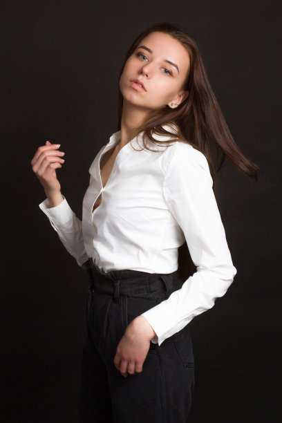 一个穿着白色衬衫和黑色牛仔裤的年轻女孩，背景是黑色的演播室图片下载