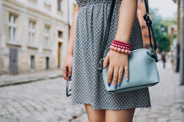 女手与蓝色手提包。女性的手与指甲和手镯拿着太阳镜。穿着有配饰的时尚女性。图片下载