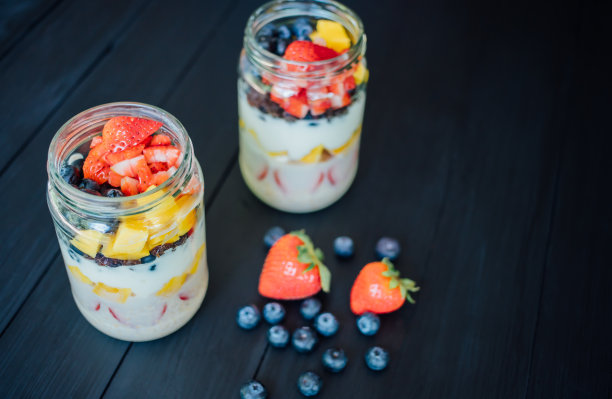 新鲜的芒果、蓝莓和草莓切片装在玻璃罐中，放在木桌上。早餐或健康食品概念，俯视图照片图片下载