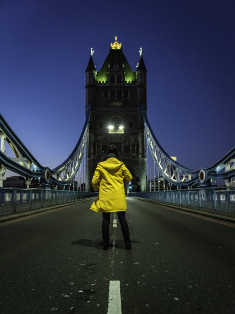 年轻女子，穿着黄色雨衣在塔桥上图片下载