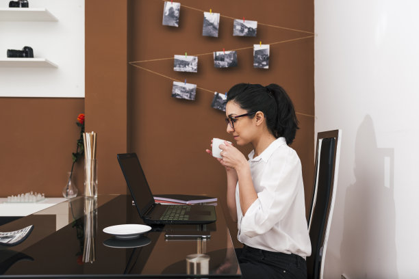 戴眼镜的年轻女子在她临时家庭办公室工作的时候正在喝咖啡休息图片下载