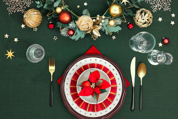 圣诞餐桌上摆放着暗红白色的盘子，红纸戒指和一品红，金色的餐具。红色，绿色和金色的镀金装饰。平铺在深绿色的亚麻纺织品背景上。图片下载