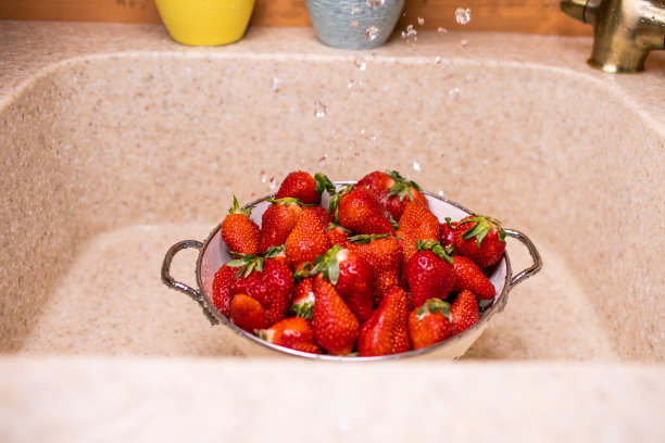 熟透的草莓放在白漏勺下，往水槽里倒水图片下载