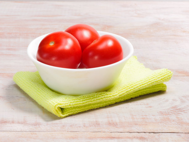 白色碗里的红番茄，绿色毛巾，棕色木质背景图片下载