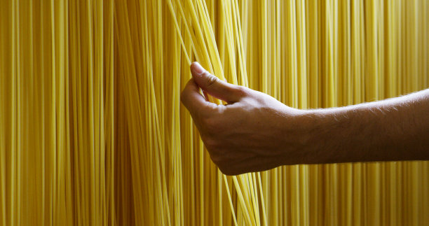 早上，一个小男孩用手触摸新鲜的意大利面，把它们晾干，以确保高质量图片下载